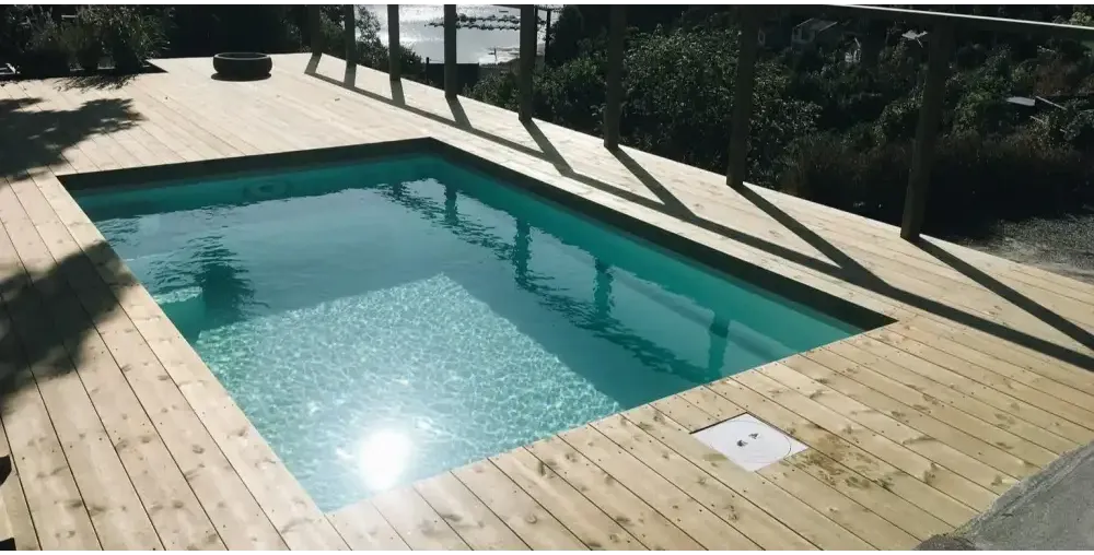 Glasfiberpool Mini Victoria med rektangulär form och klart turkost vatten omgivet av ljus trädeck